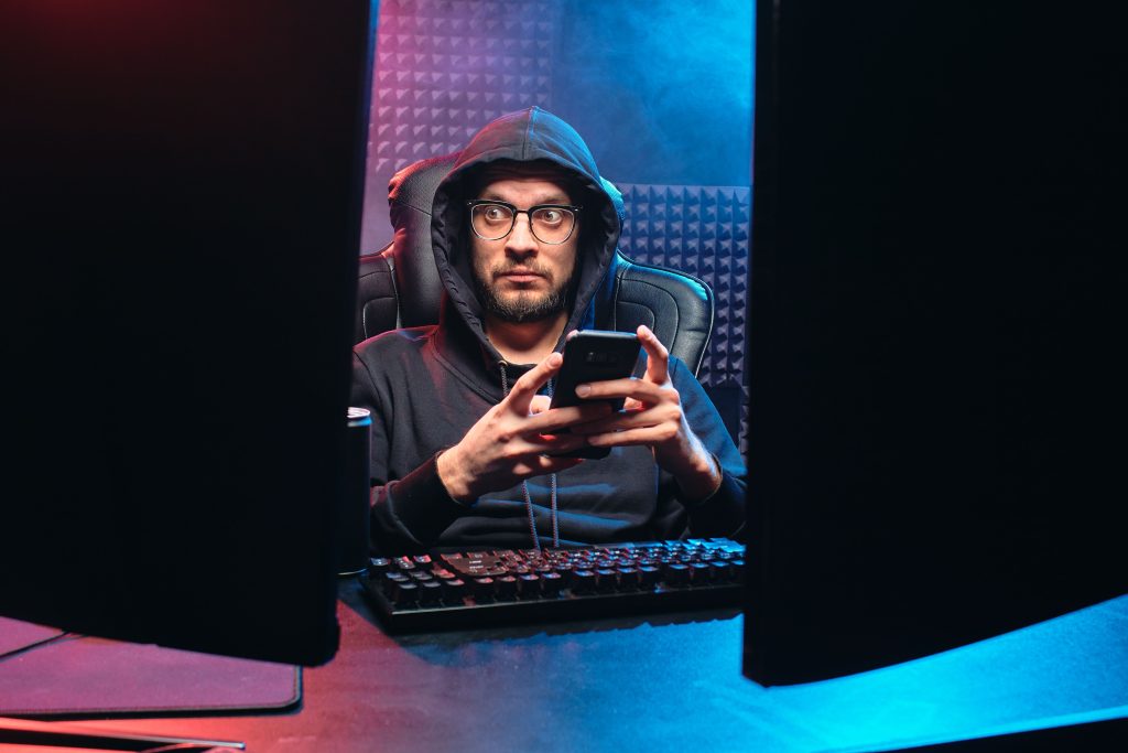 Hooded hacker using a smartphone to carry out a cyber attack in a dark room
